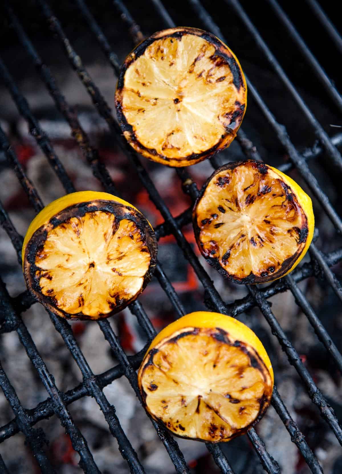 Halved lemons face up on a grill showing grill marks on the cut surface from caramelizing the natural sugars for grilled citrus sauce to serve with seafood