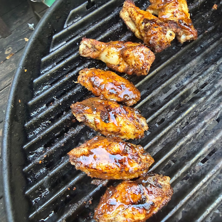 Chicken wings seasoned with fresh-ground Scout Fire grilling over coals, being basted with green cayenne hot honey sauce