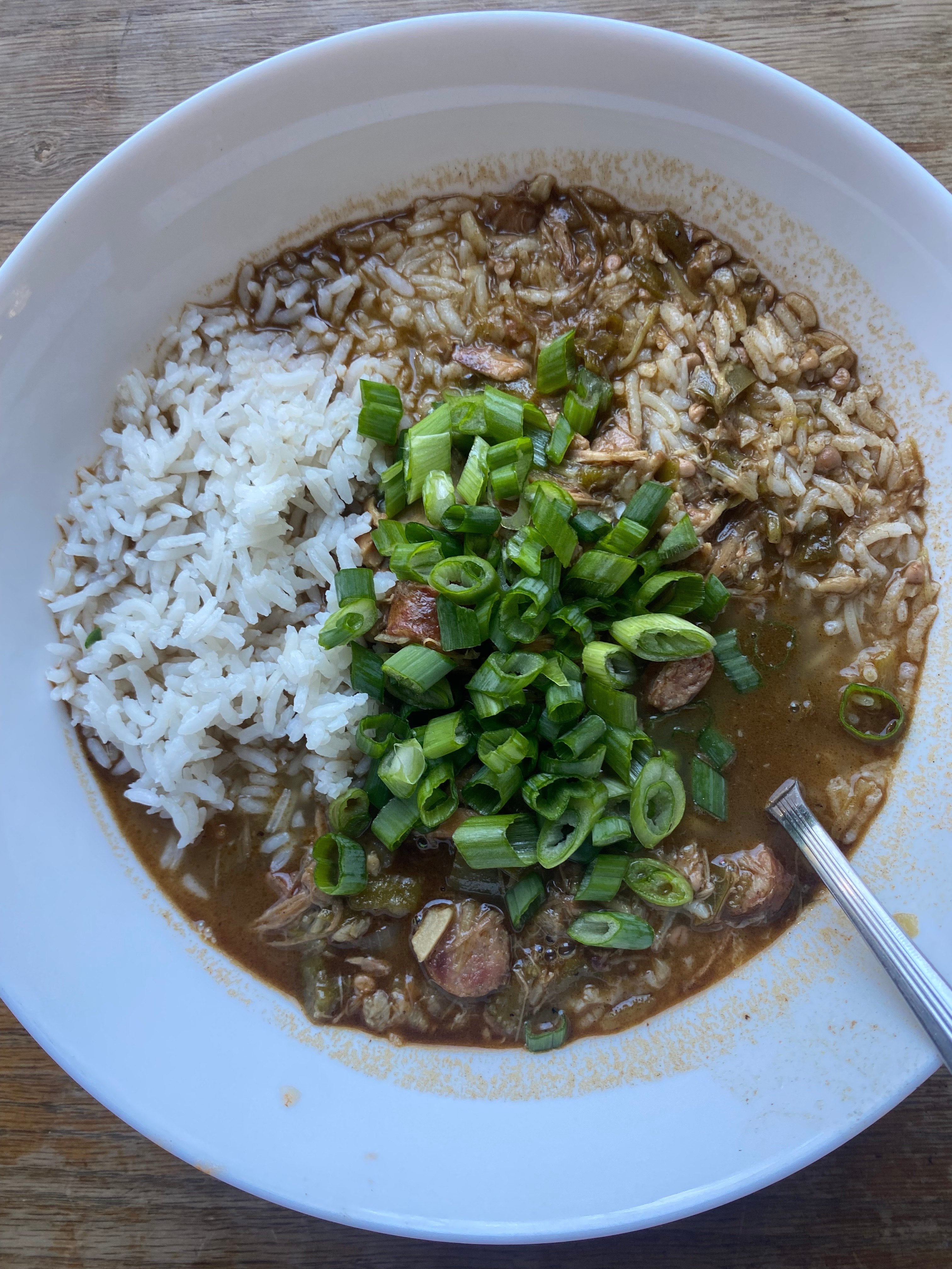 Close up of a bowl of Cajun andouille chicken gumbo showing fluffy basmati rice, tender pulled chicken, sliced andouille sausage, and sliced green onion garnish made with Lucky Cajun Black Label fresh ground Cajun seasoning and a dark corn oil roux