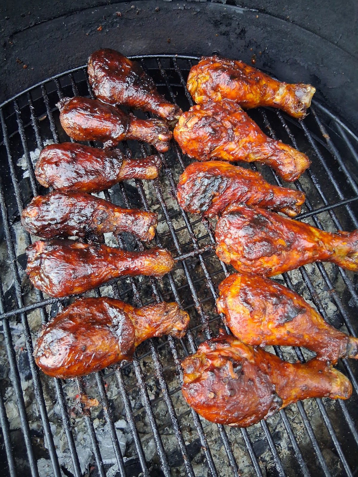 BBQ jerk chicken legs on a smoker glazed with guava sauce seasoned with Lucky Cajun What A Jerk fresh ground jerk seasoning showing the dark aromatic crust from a 24 hour marinade and low and slow smoke