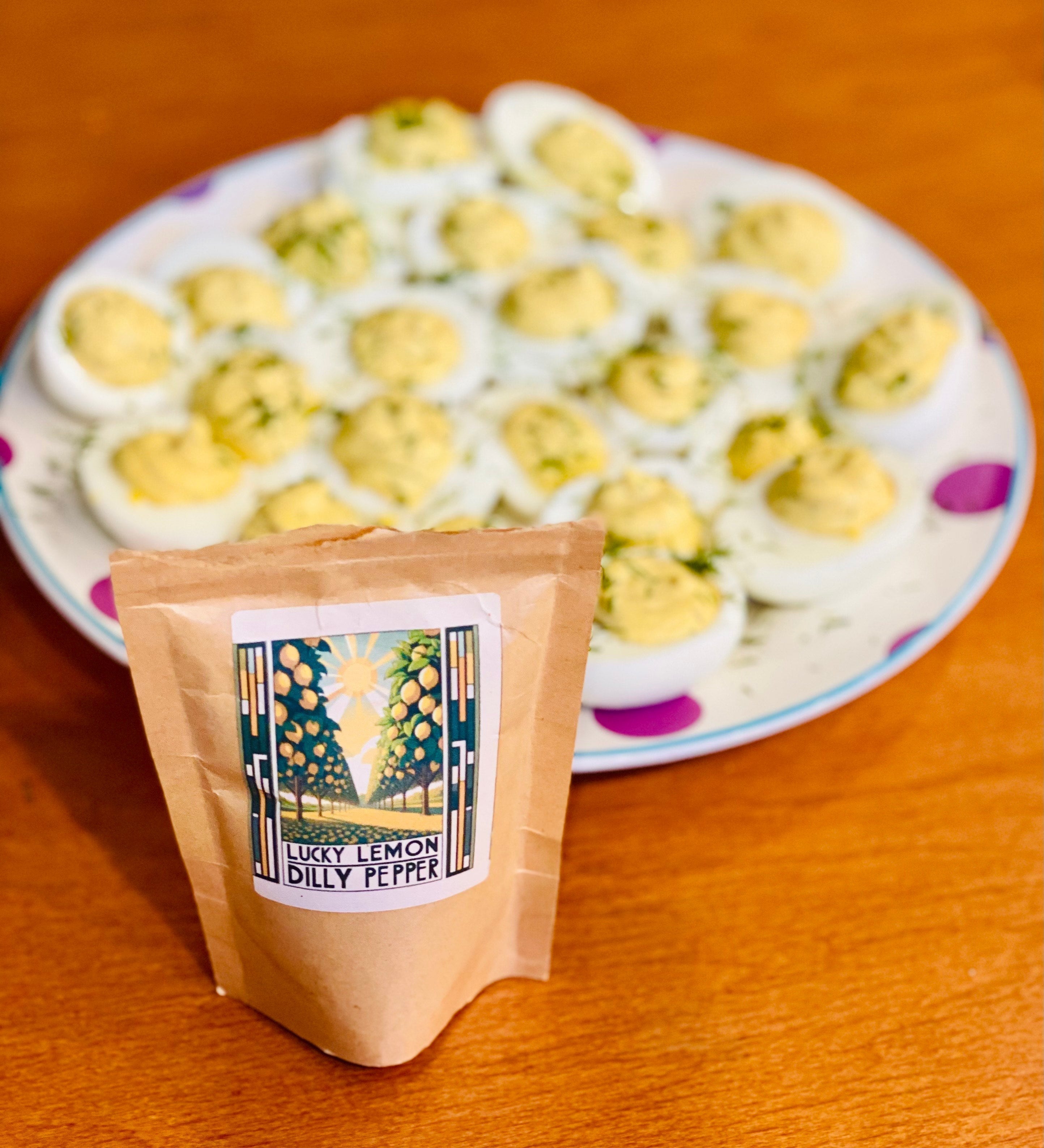 Plate of Lucky Lemon Dilly Pepper deviled eggs in the background with an open bag of Lucky Cajun Lucky Lemon Dilly Pepper fresh ground seasoning in the foreground showing the citrusy herb blend that makes these deviled eggs disappear