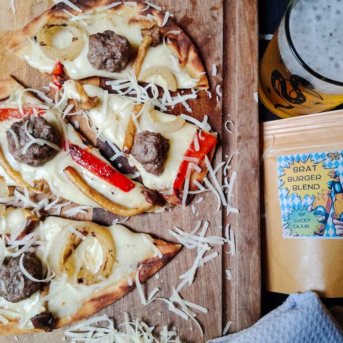 Brat burger flatbread with grilled onion mushrooms and red bell pepper on creamy mustard cream sauce with bubbly golden Fontina cheese on a cutting board seasoned with Lucky Cajun Brat Burger Seasoning