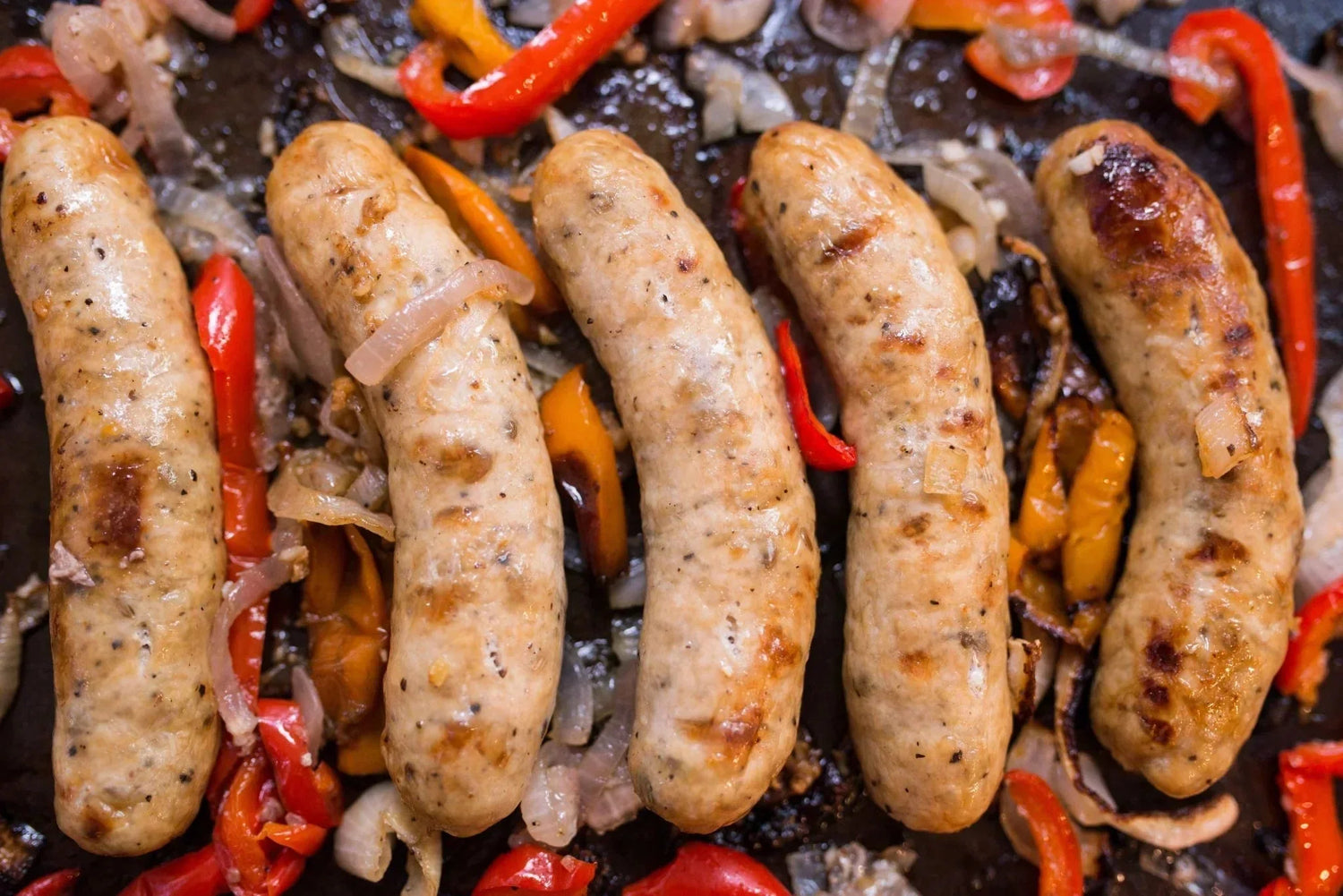 Roasted bratwurst with sautéed bell peppers and onions made with Lucky Cajun Brat Burger fresh ground seasoning showing the caramelized crust and topping combinations for the ultimate brat burger
