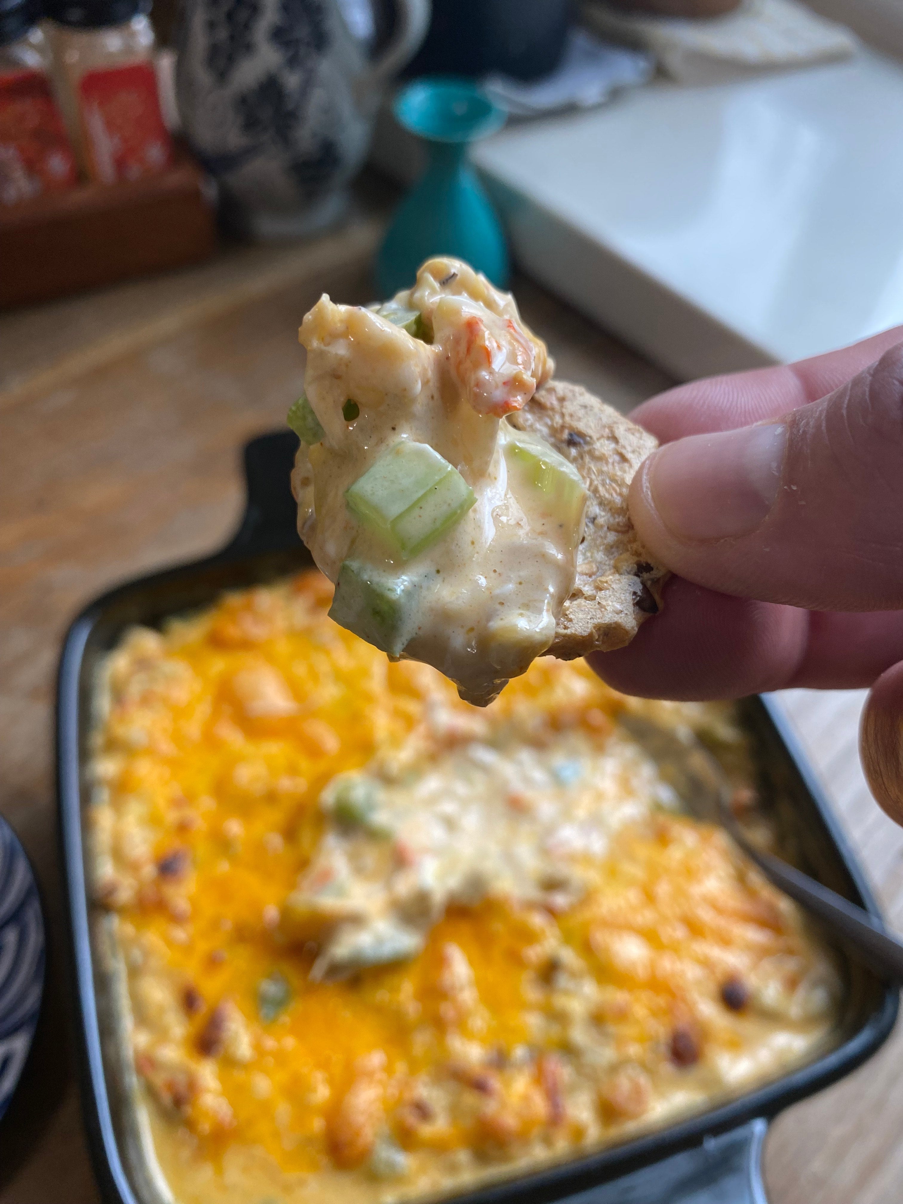 Close up of bubbly golden crawfish artichoke dip on a cracker showing the creamy Cajun seasoned filling with Lucky Cajun Black Label fresh ground seasoning and melted sharp cheddar topping