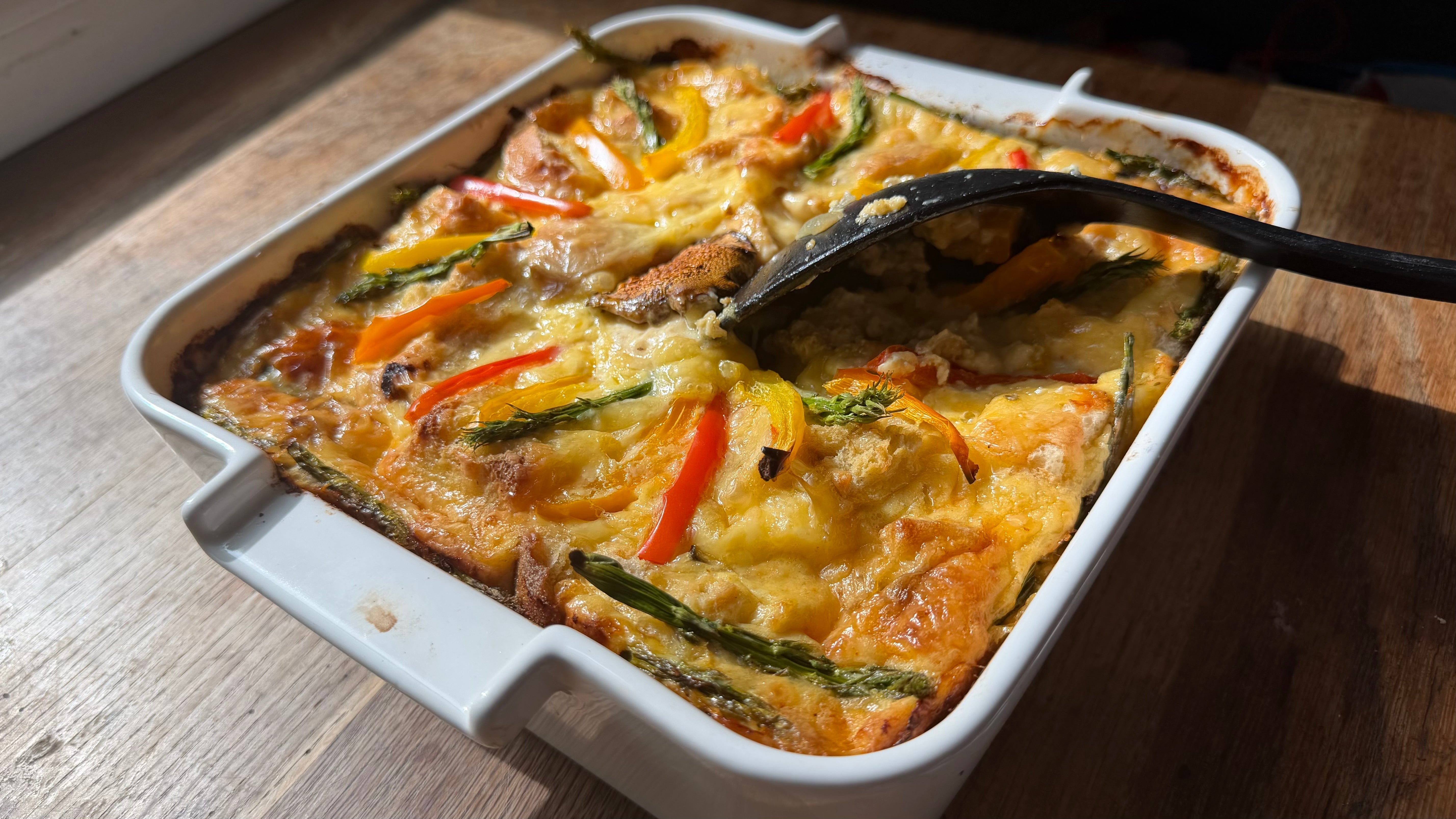 Breakfast casserole with a spoon scooping out a golden baked egg custard layered with vegetables cheese and bread seasoned with Lucky Cajun Black Label on a wooden table