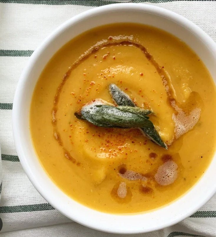 Bowl of creamy roasted butternut squash soup topped with brown butter fried sage on a striped tablecloth, seasoned with Lucky Cajun Black Label.