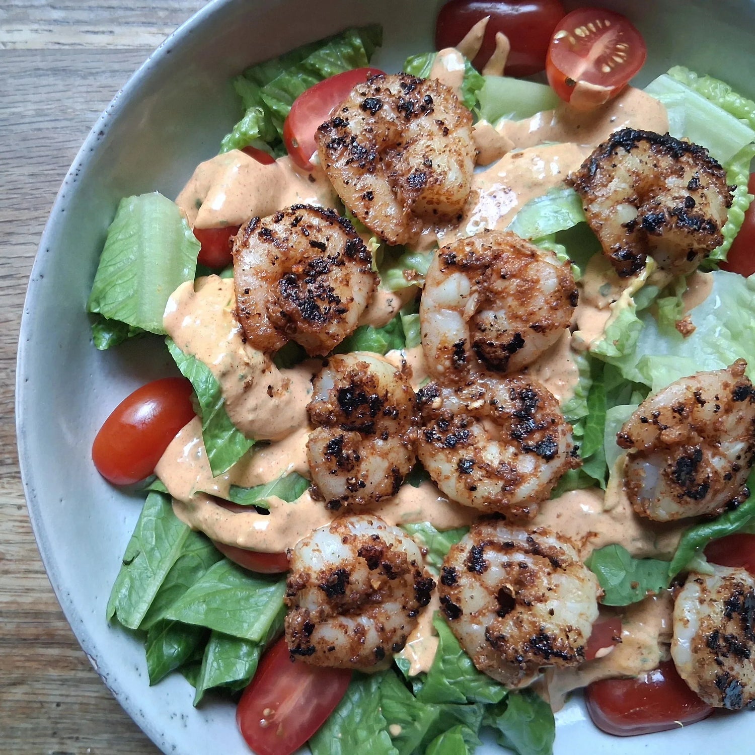 Blackened shrimp on romaine salad with tomatoes drizzled with Sneaky Sauce Cajun remoulade showing the bold contrast between the charred seasoned shrimp and creamy sauce