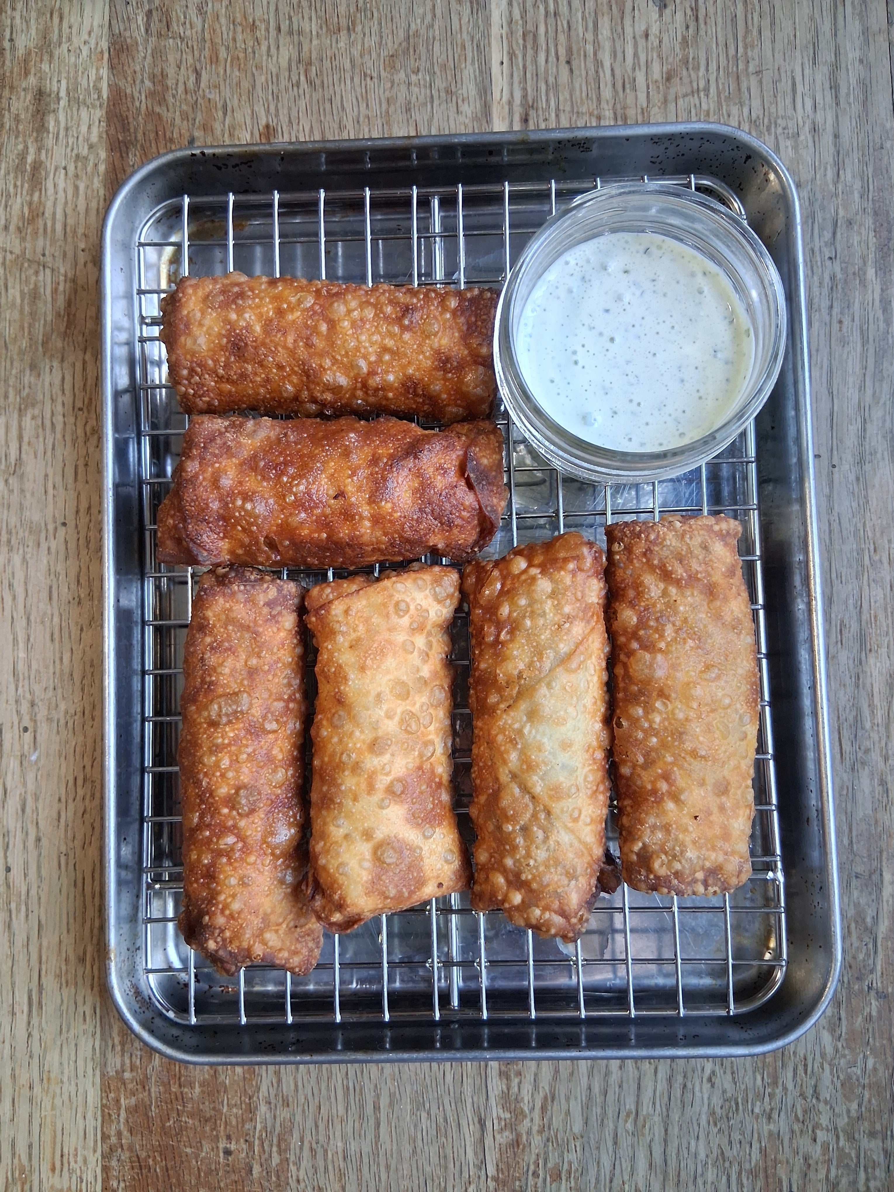 Crispy taco beef egg rolls with cilantro lime crema dipping sauce on a stainless steel sheet pan, made with Lucky Cajun Taco Tuesday seasoning.