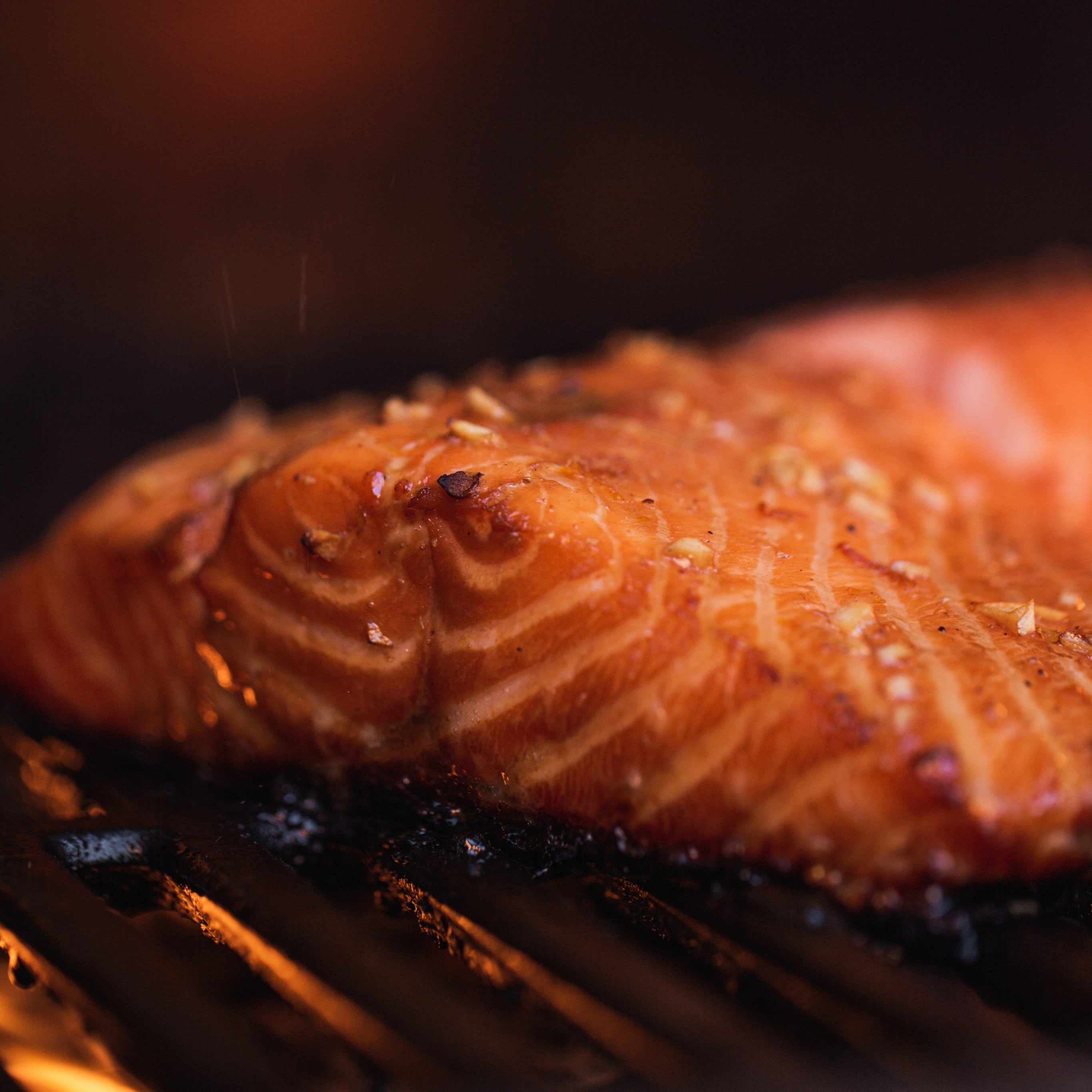 Close-up of fire roasted salmon on cast iron grill grates with a charred crust, seasoned with Lucky Cajun Bay Bae bay seasoning.