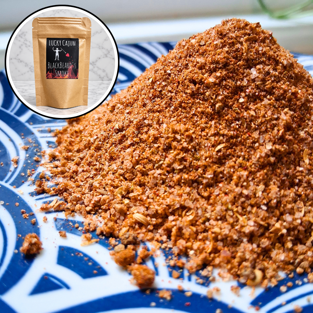 A close-up of a pile of reddish-brown seasoning or spice blend on a blue-and-white patterned plate, with a circular inset showing a kraft pouch labeled Lucky Cajun Blackened Seasoning.