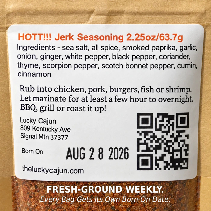 A close-up of a kraft paper spice jar showing a white label for Lucky Cajun Jerk Seasoning. The label includes product details, ingredients, a QR code, and ground spice visible through the clear lower section of the jar.