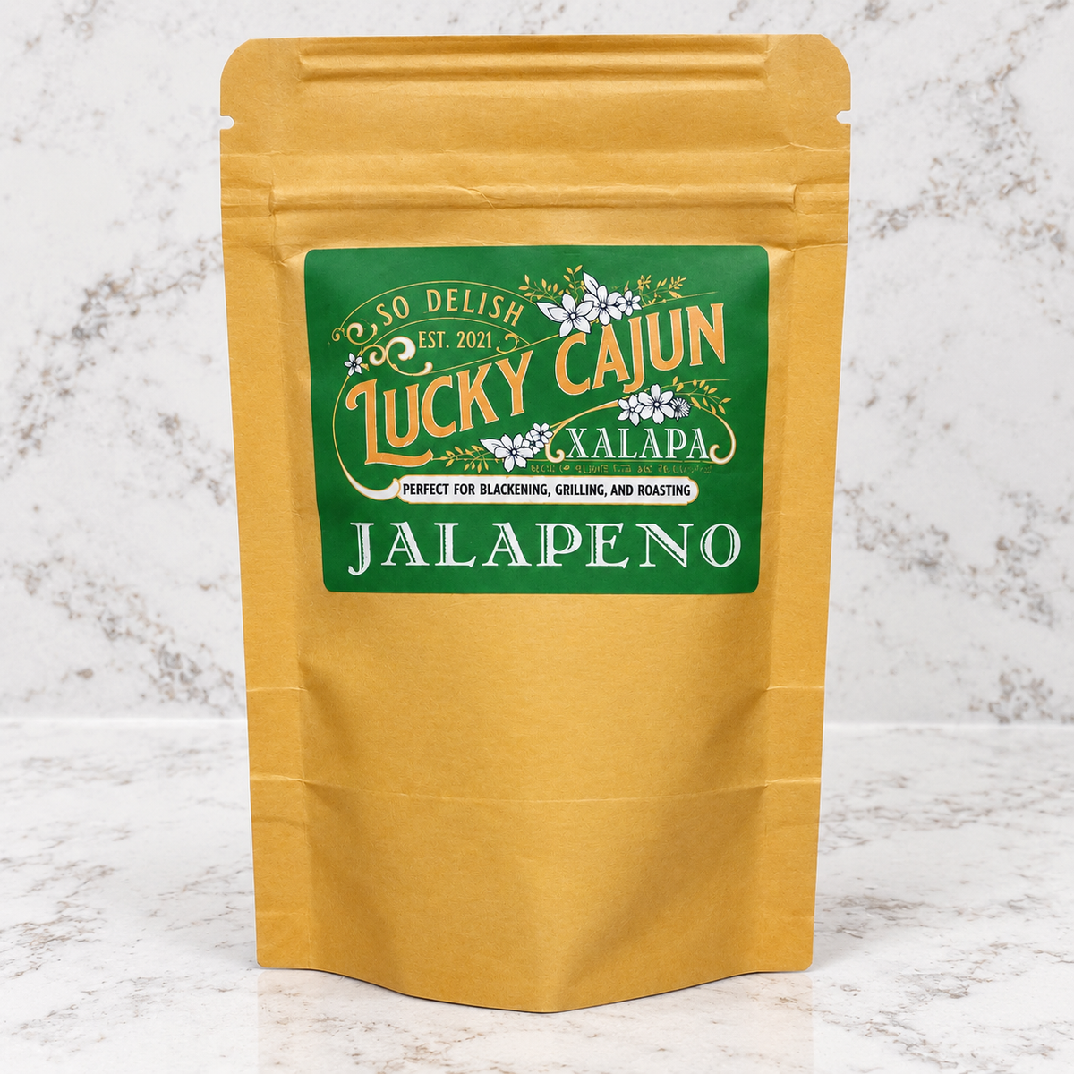 A gold-colored stand-up pouch of Lucky Cajun Jalapeño seasoning, featuring a green label with white and gold lettering, set against a white marble background.