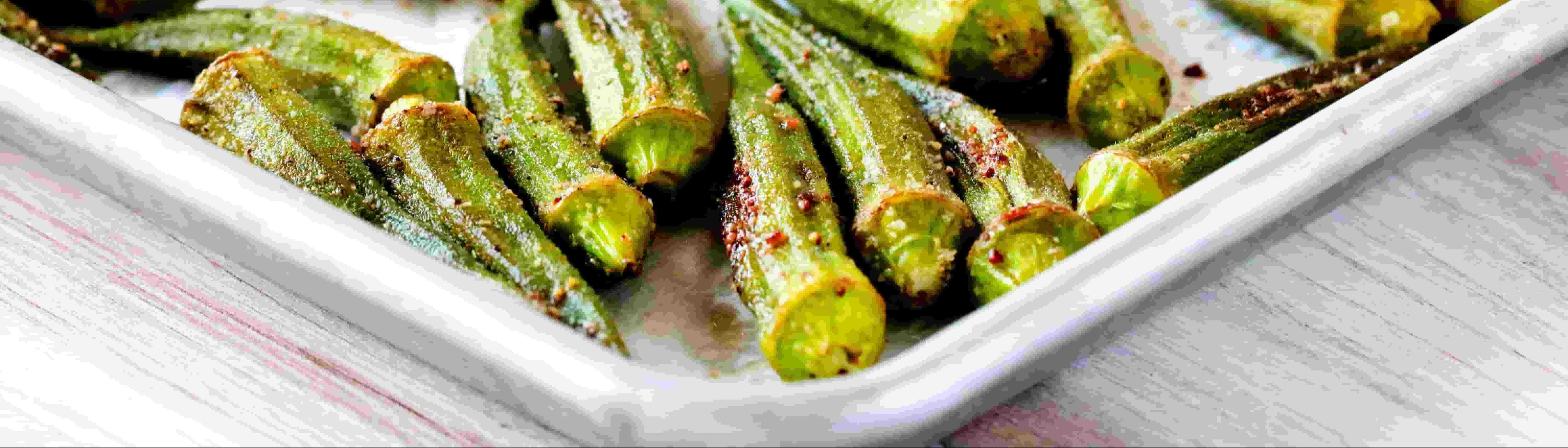 Roasted okra on a white plate with a wooden surface underneath
