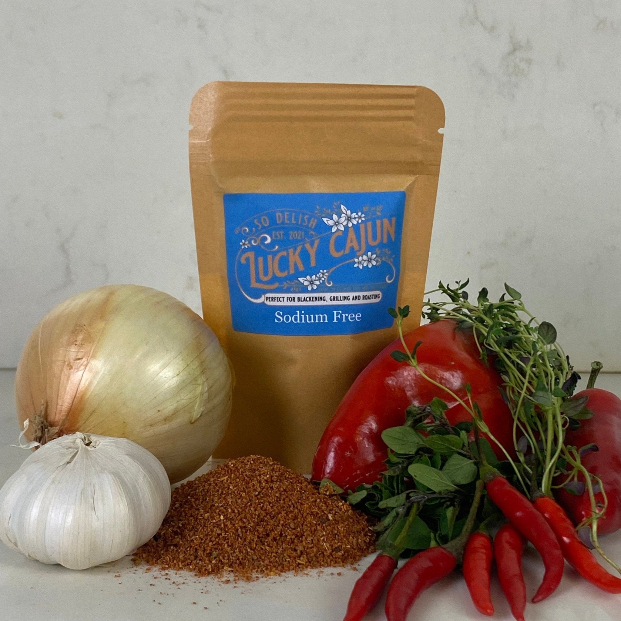 A pouch of Lucky Cajun Salt-Free Original seasoning surrounded by fresh white onions, garlic, and red peppers—highlighting the fresh, small-batch ingredients used in this sodium-free blend.