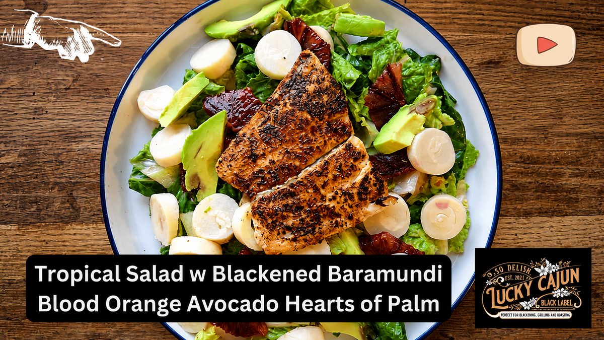 Assembled tropical salad with blackened barramundi on a white plate on a wooden table, topped with blood orange, avocado and hearts of palm, seasoned with Lucky Cajun Voodoo.