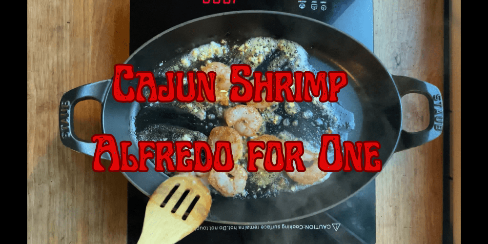 Cajun shrimp searing in a cast iron pan with a wooden spoon showing Lucky Cajun Black Label fresh ground seasoning blooming on contact with hot garlic butter for Cajun shrimp alfredo