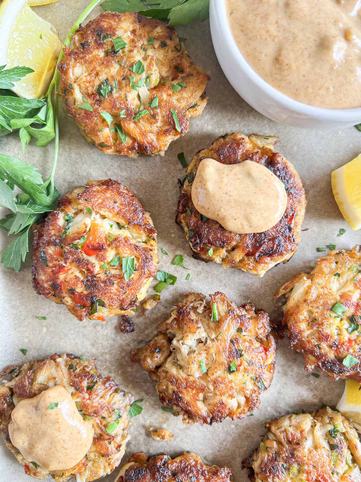 Crab cakes on a sheet pan served with Sneaky Sauce Cajun remoulade showing the golden crust and bold contrast sauce from the No-BS Seafood Cookbook