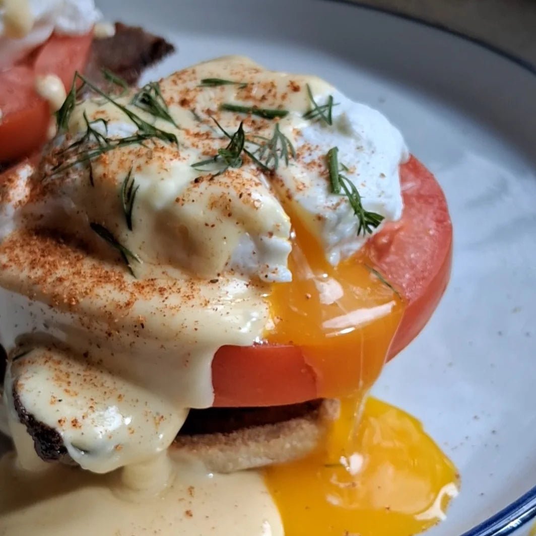 Close-up of Eggs Hussarde with a cut poached egg, yolk running down over tasso and tomato onto the plate, garnished with hollandaise and Lucky Cajun Black Label seasoning.