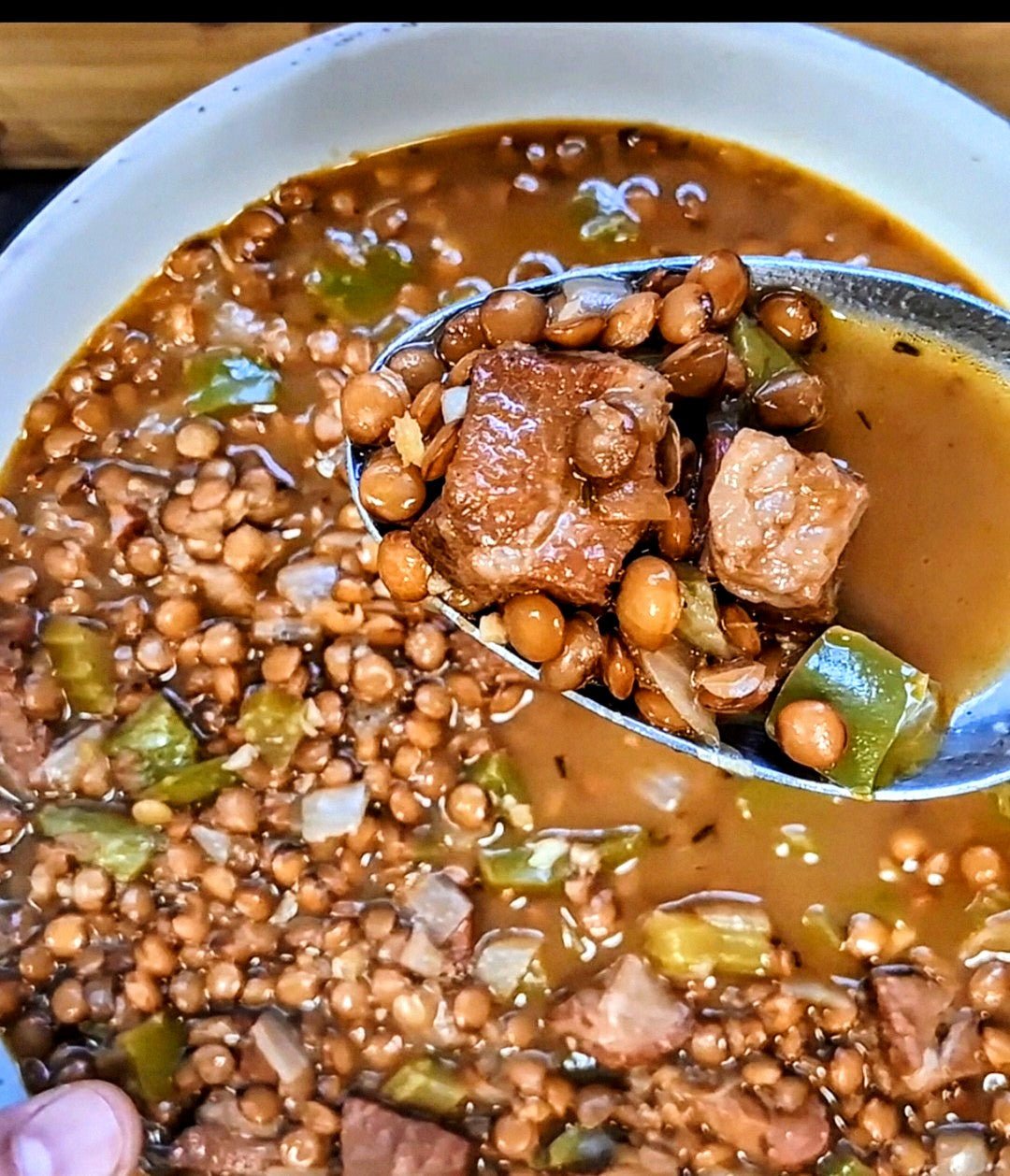 Close up of a spoon full of hearty brown lentil soup with tasso and Lucky Cajun Black Label fresh ground Cajun seasoning showing the rich deeply flavored broth and tender lentils from a classic Lucky Cajun restaurant recipe
