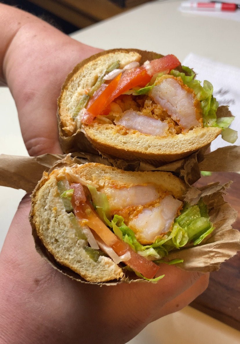 Cross-section of a Cajun shrimp po'boy on a French loaf showing crispy fried shrimp, lettuce, tomato, pickles, and remoulade sauce — seasoned with Lucky Cajun Black Label.