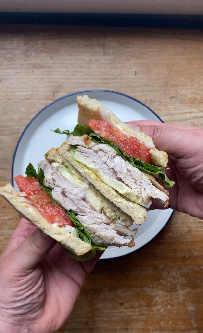 Cross-section of a turkey avocado sandwich on toasted sourdough showing layers of roasted turkey, brie, avocado, lettuce, tomato and Dijonnaise — seasoned with Lucky Cajun Black Label.