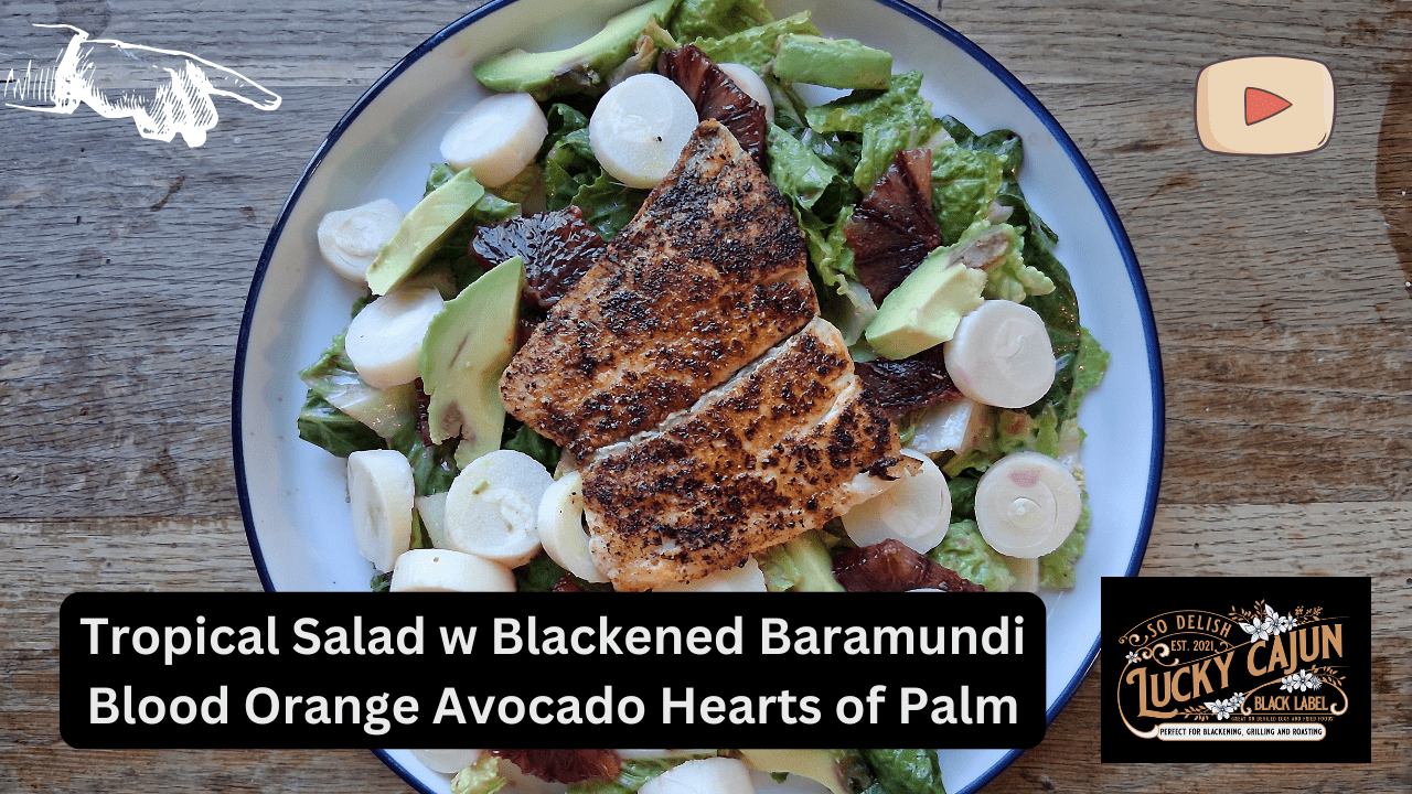 Assembled tropical salad with blackened barramundi on a white plate on a wooden table, topped with blood orange, avocado and hearts of palm, seasoned with Lucky Cajun Voodoo.