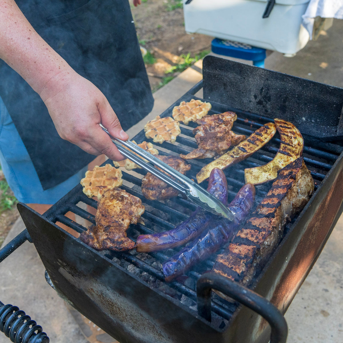 Pork loin, eggplant, and chicken breast seasoned with fresh-ground Spicy Italian Grandma, grilling over an open flame
