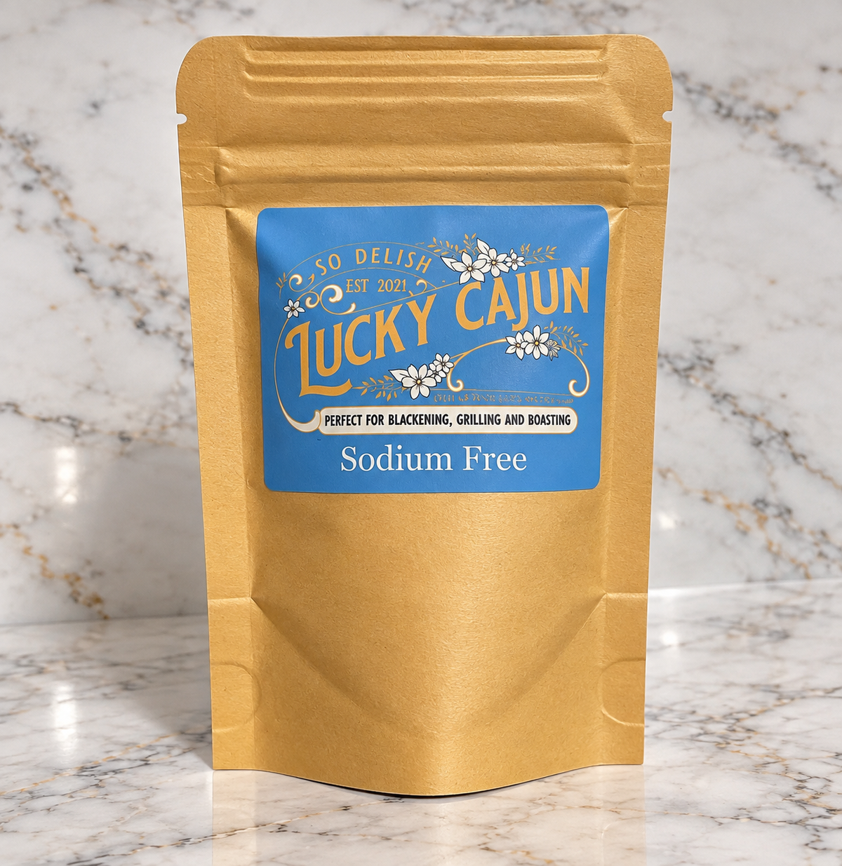 A gold-colored stand-up pouch of Lucky Cajun Sodium Free seasoning, featuring a blue label with white floral accents, set against a white marble background.