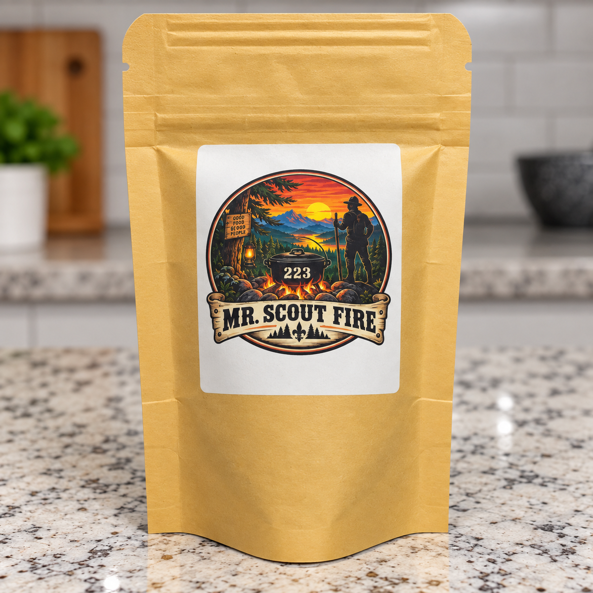 A gold stand-up pouch with a white label reading "223 MR. SCOUT FIRE" and a camping-themed illustration, standing on a granite countertop in a kitchen setting.