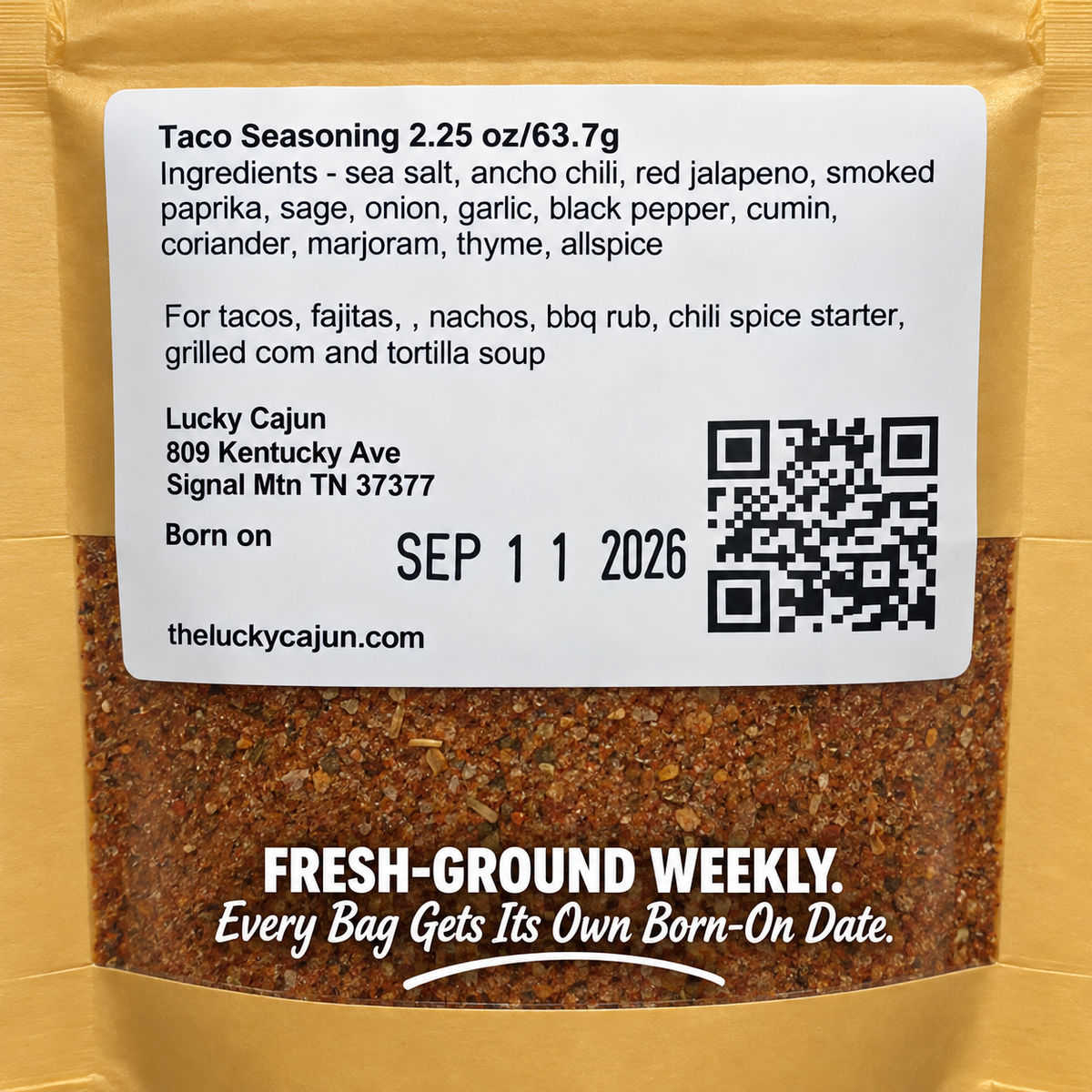 A bag of Lucky Cajun Taco Seasoning with a large white label showing ingredients, address, birth date, and QR code, over a gold pouch with visible ground seasoning through the clear lower section.