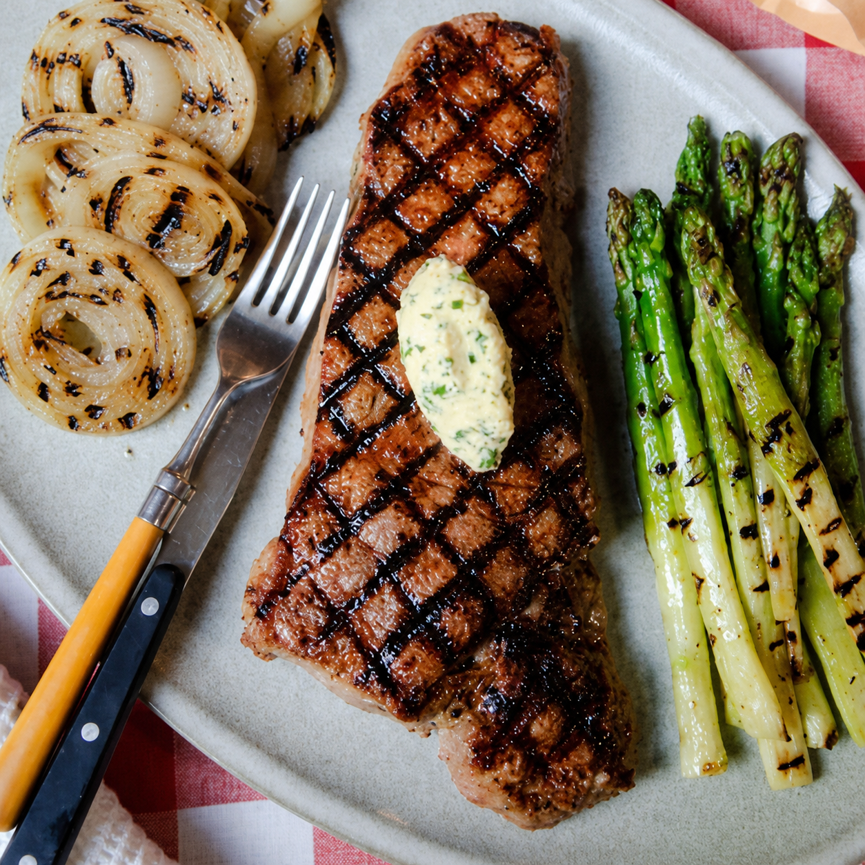 Grilled NY Strip steak seasoned with Lucky Cajun Black Label, topped with herb compound butter, and served with grilled asparagus and onions. Premium fresh-ground steak rub.