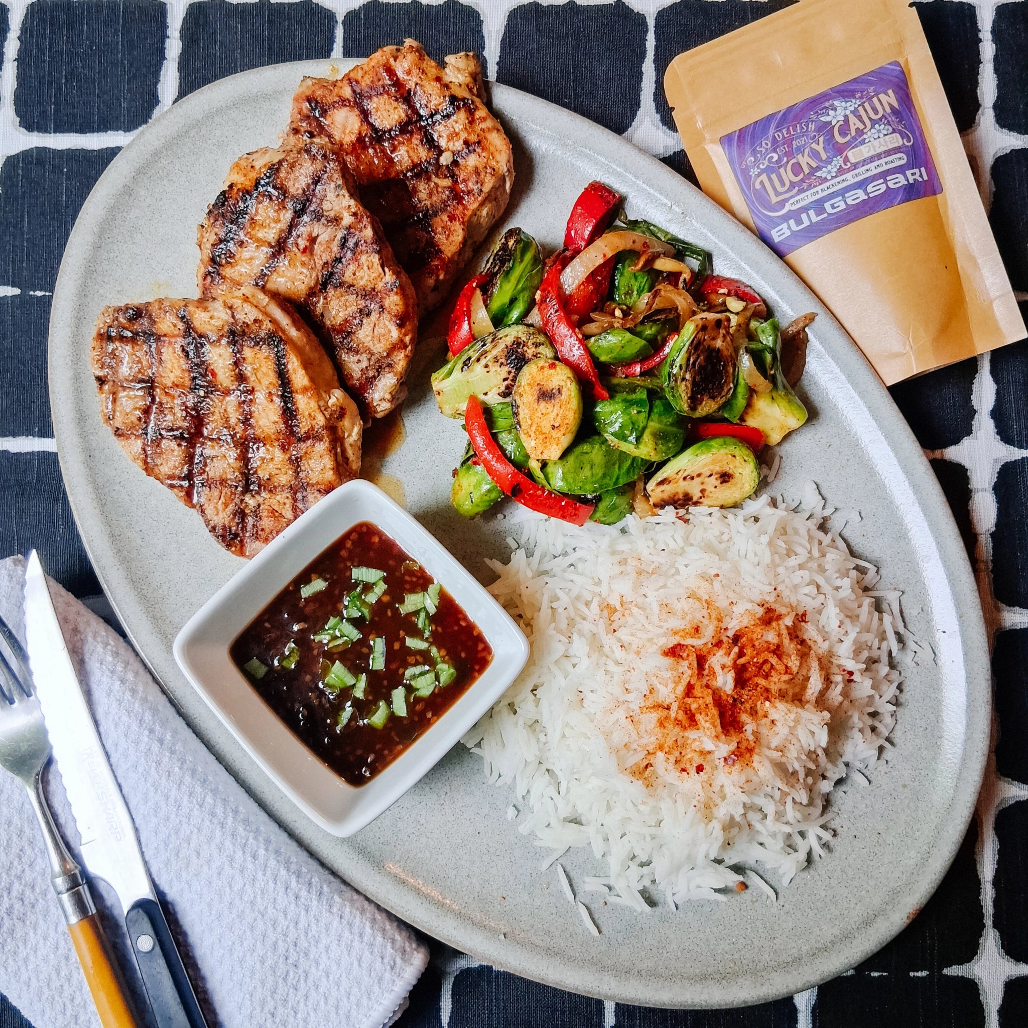 Grilled pork chops seasoned with Bulgasari Cajun-Korean fusion spice, served with stir-fried Brussels sprouts, steamed rice, and a sesame soy glaze. Small-batch umami seasoning with a Born On Date.