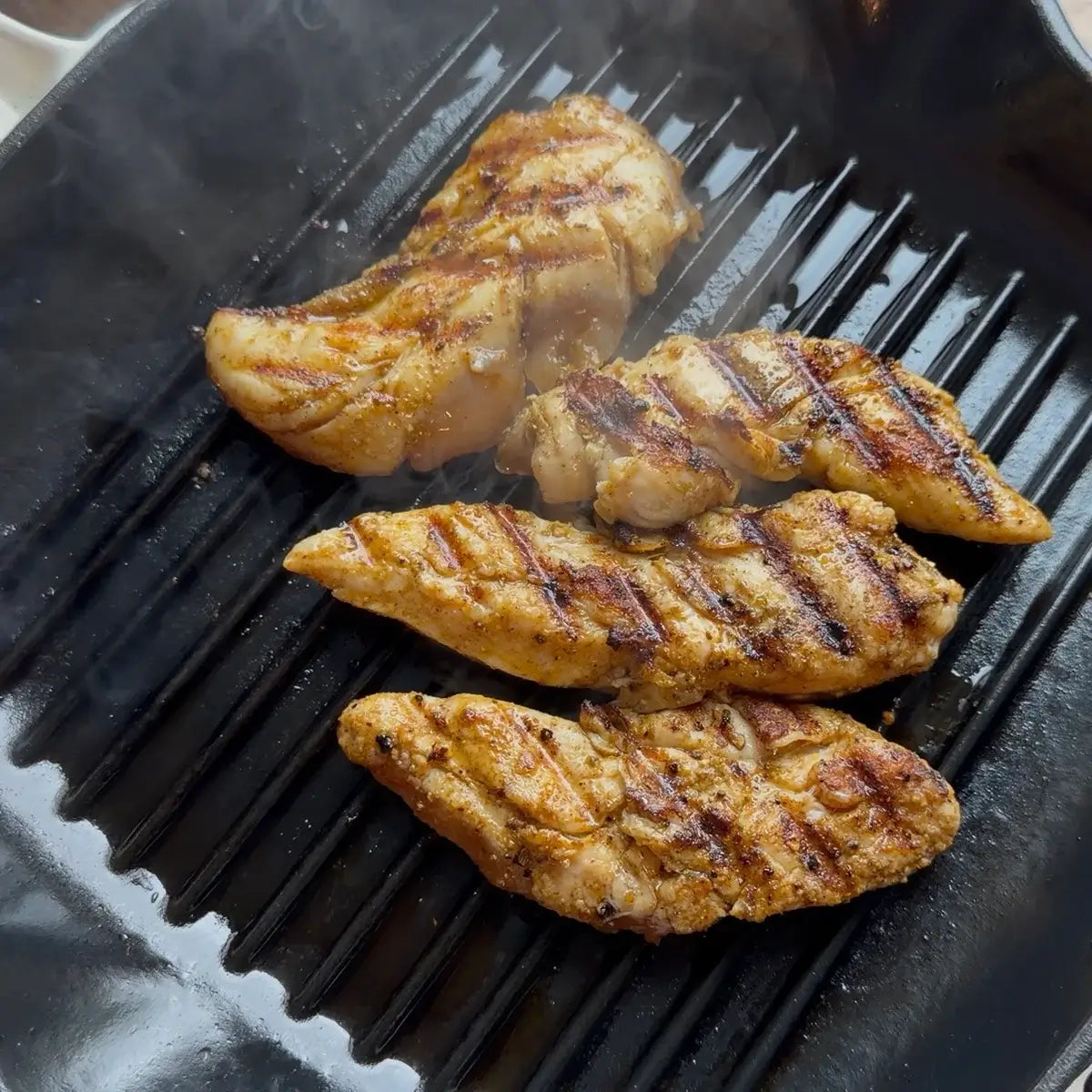 Chicken tenders grilling in a cast iron pan with Lucky Cajun fresh-ground seasoning.