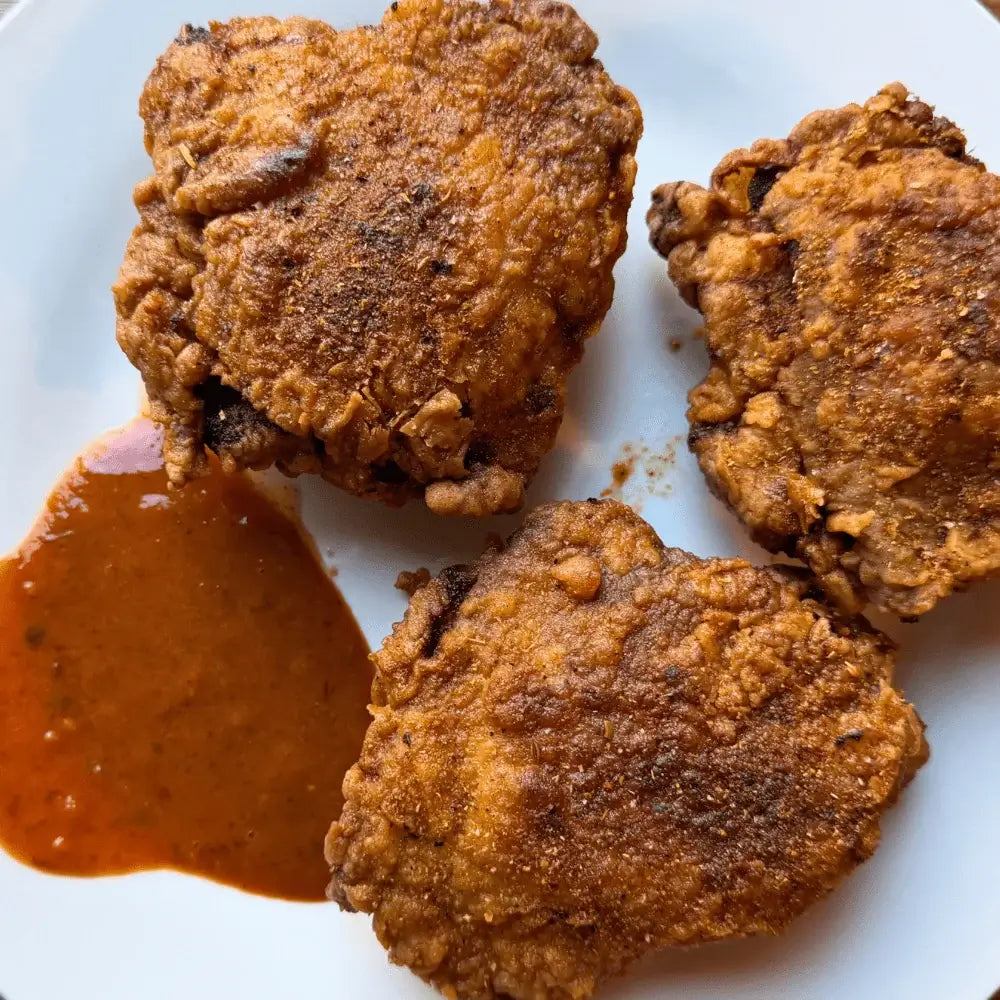 Three extra crispy fried chicken thighs with orange chipotle sauce on a white plate seasoned with Lucky Cajun.