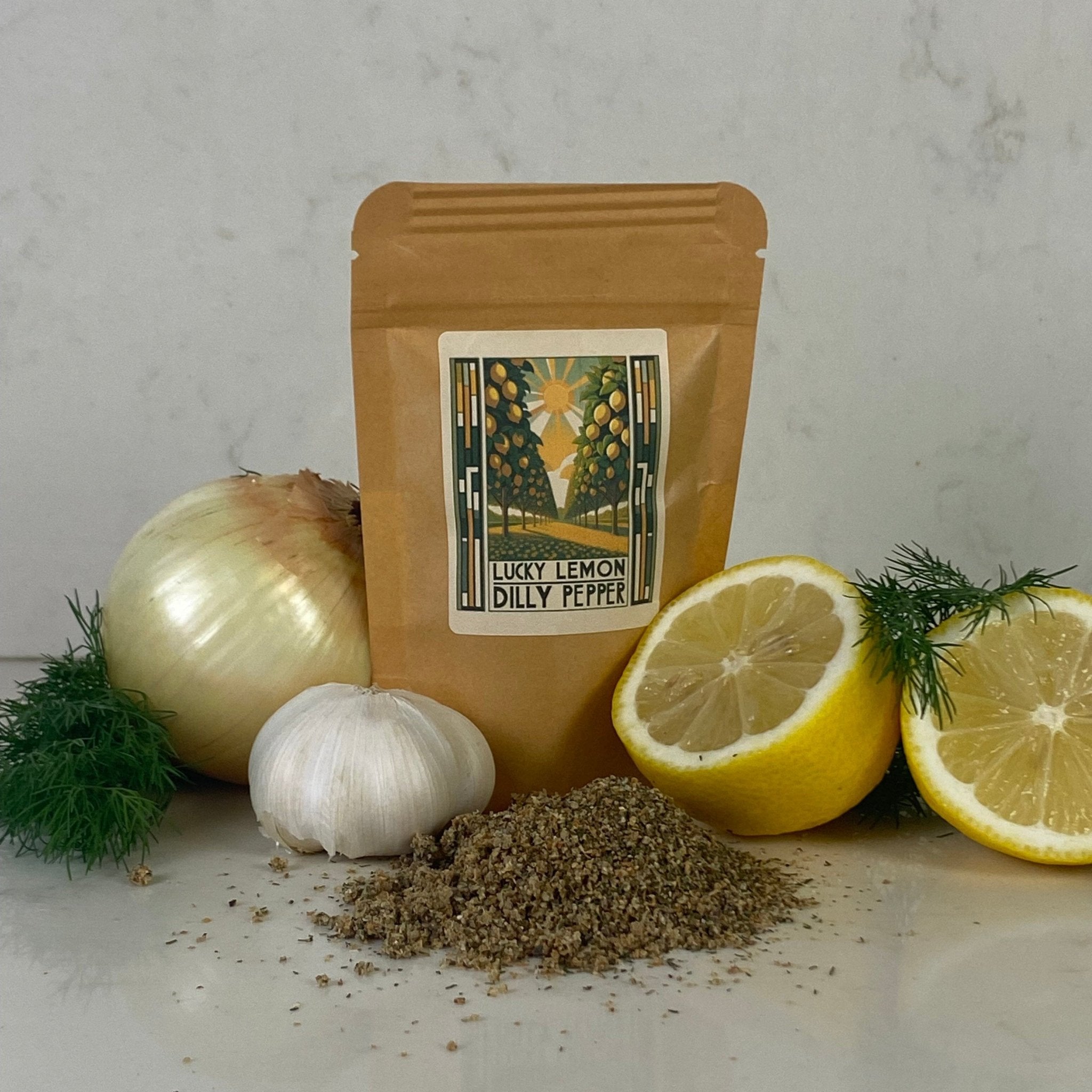 A pouch of Lucky Lemon Dilly Pepper seasoning surrounded by fresh lemon halves, white onions, garlic, and sprigs of dill—highlighting the real-fruit ingredients and handcrafted quality.